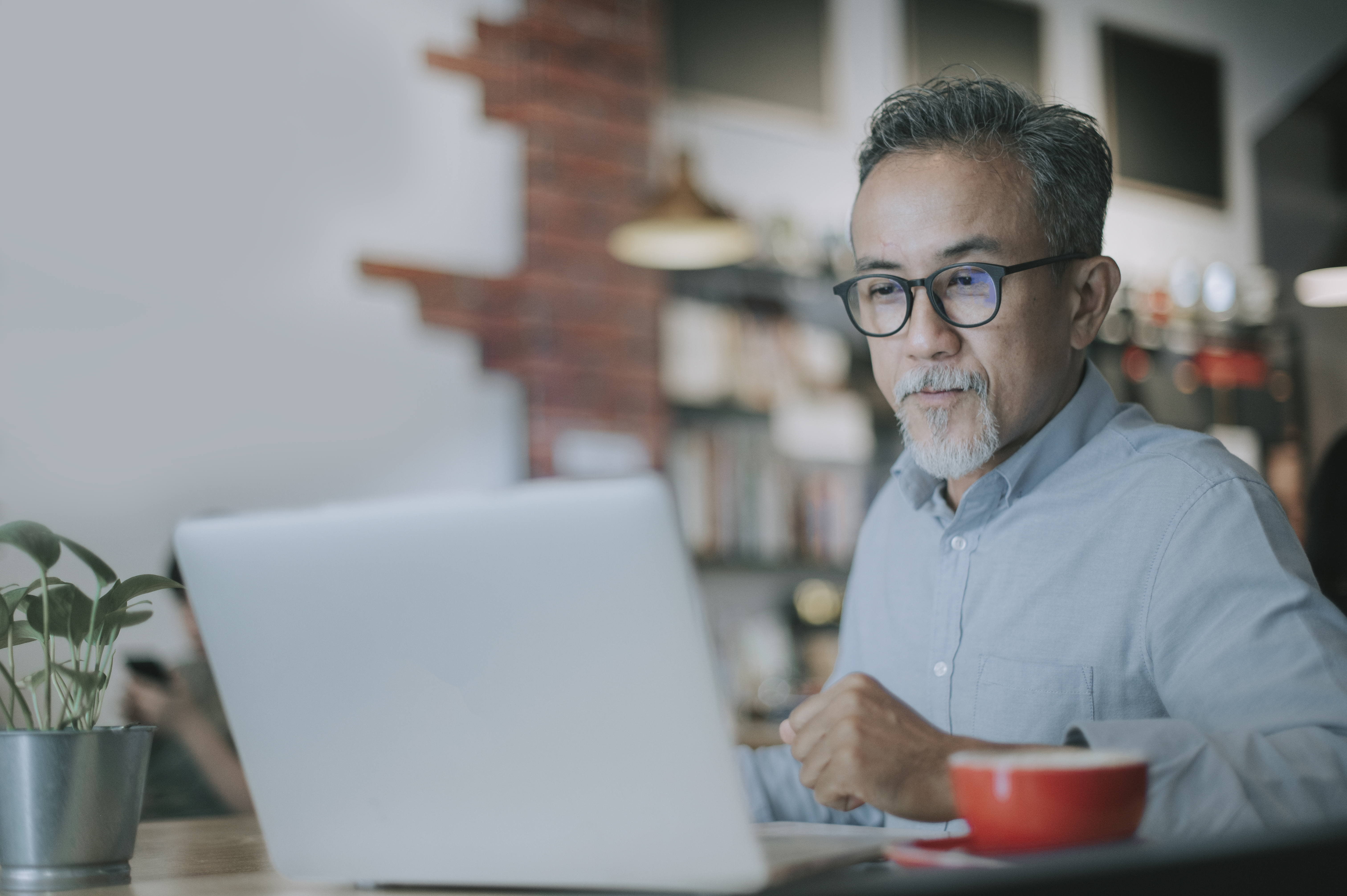 An Asian Chinese man looking at a laptop screen in a cafe