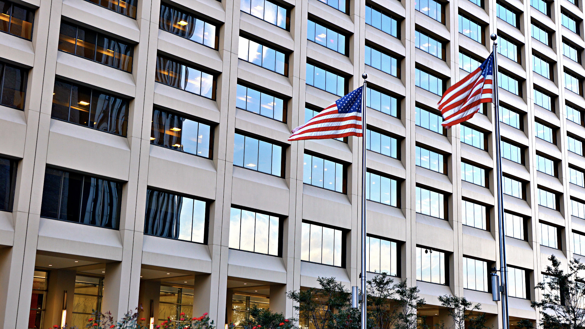Two American flags waving in front of a modern office building.