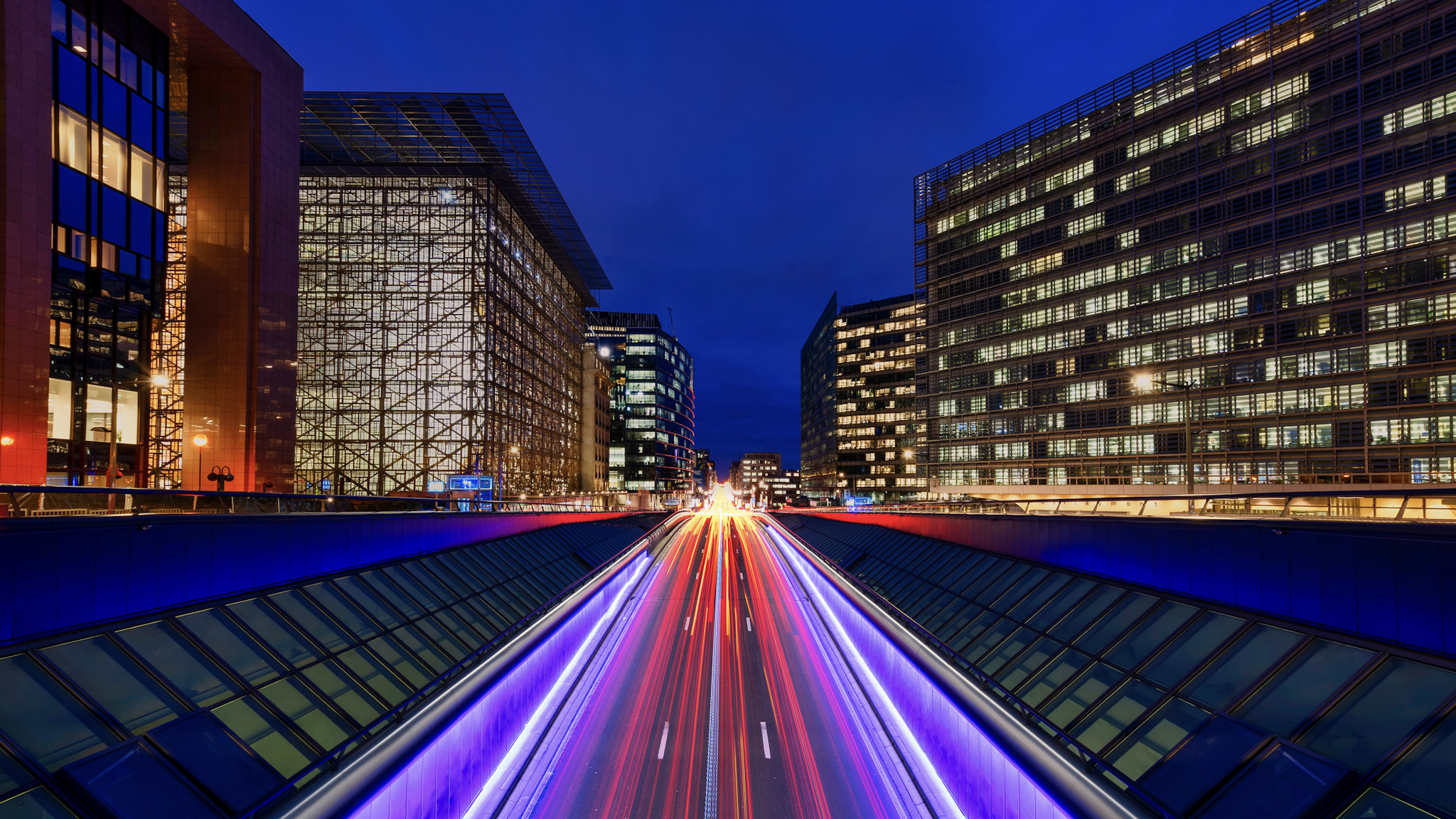 Car lights traveling fast in a dark night through a street surrounded by buildings
