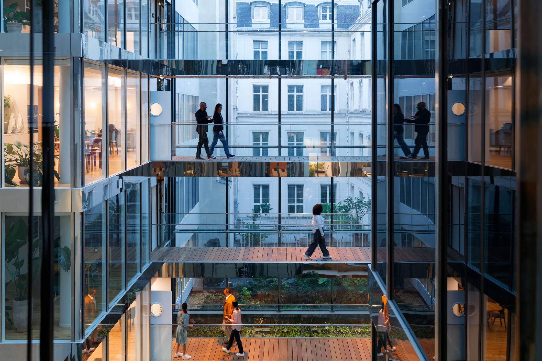 Alt Text (131 characters)
Professionals walking across glass-walled office balconies in a modern multi-storey building, representing enterprise collaboration and partnership