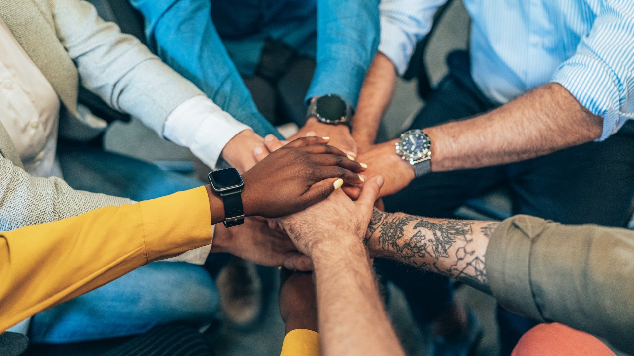 Hands overlapping in the center as people gather in a huddle.