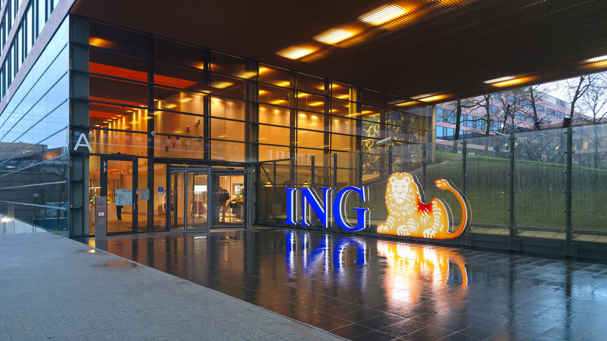 Ingresso moderno della sede ING con facciata in vetro illuminata e il logo della banca ben visibile