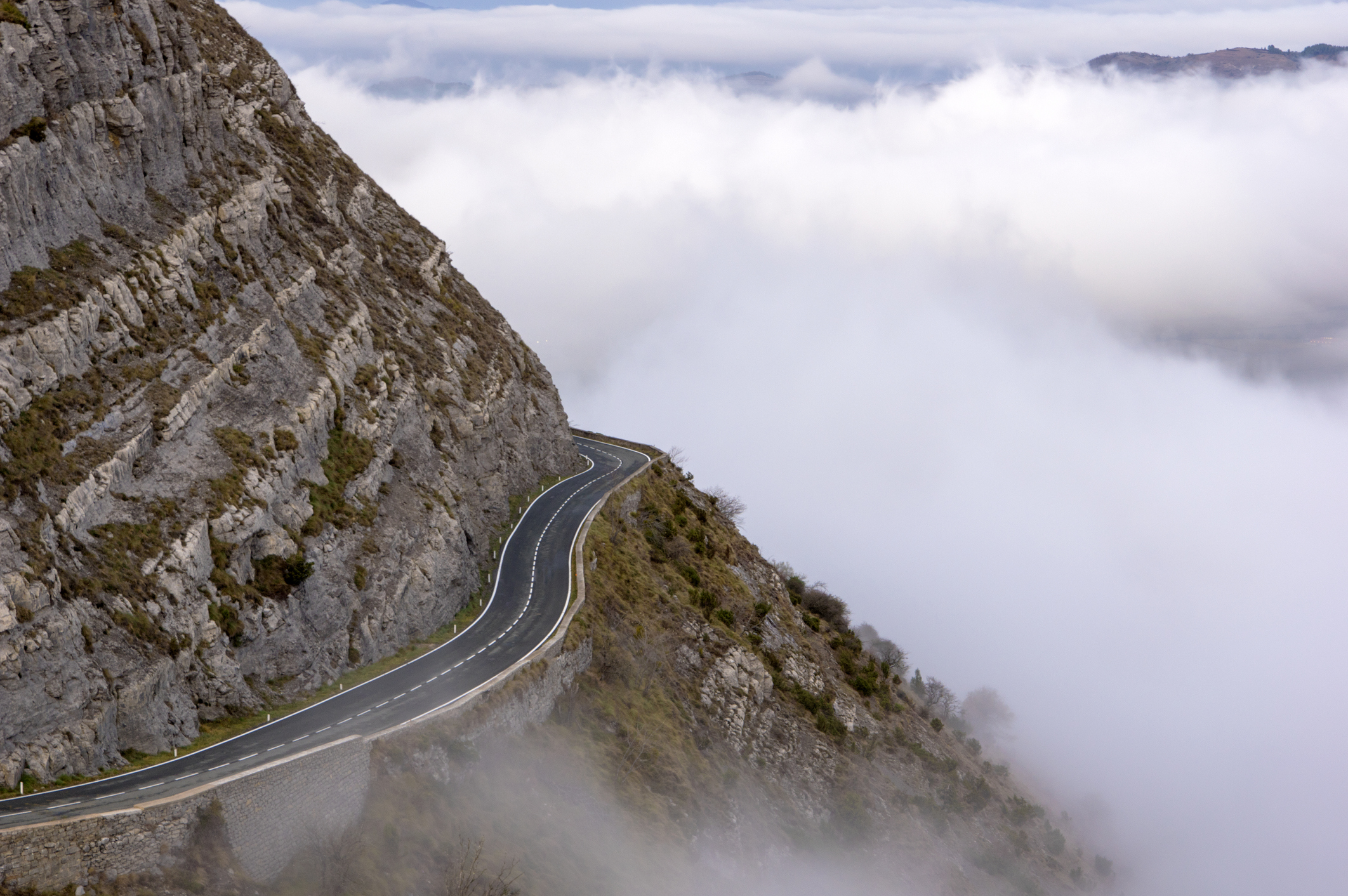 Road wrapping around mountain with clouds in background