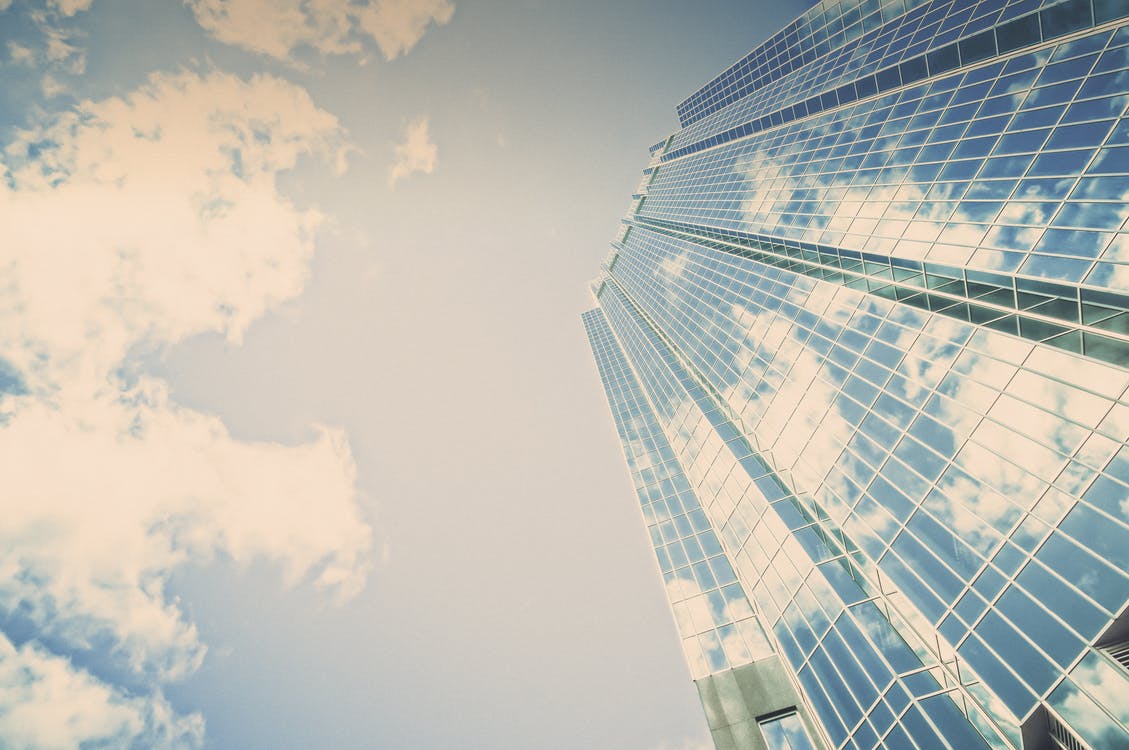 A very reflective sky scraper has clouds and a bright blue sky reflecting off of it in the daytime.