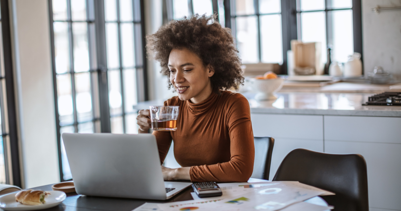 Woman sipping tea while working on laptop from kitchen table