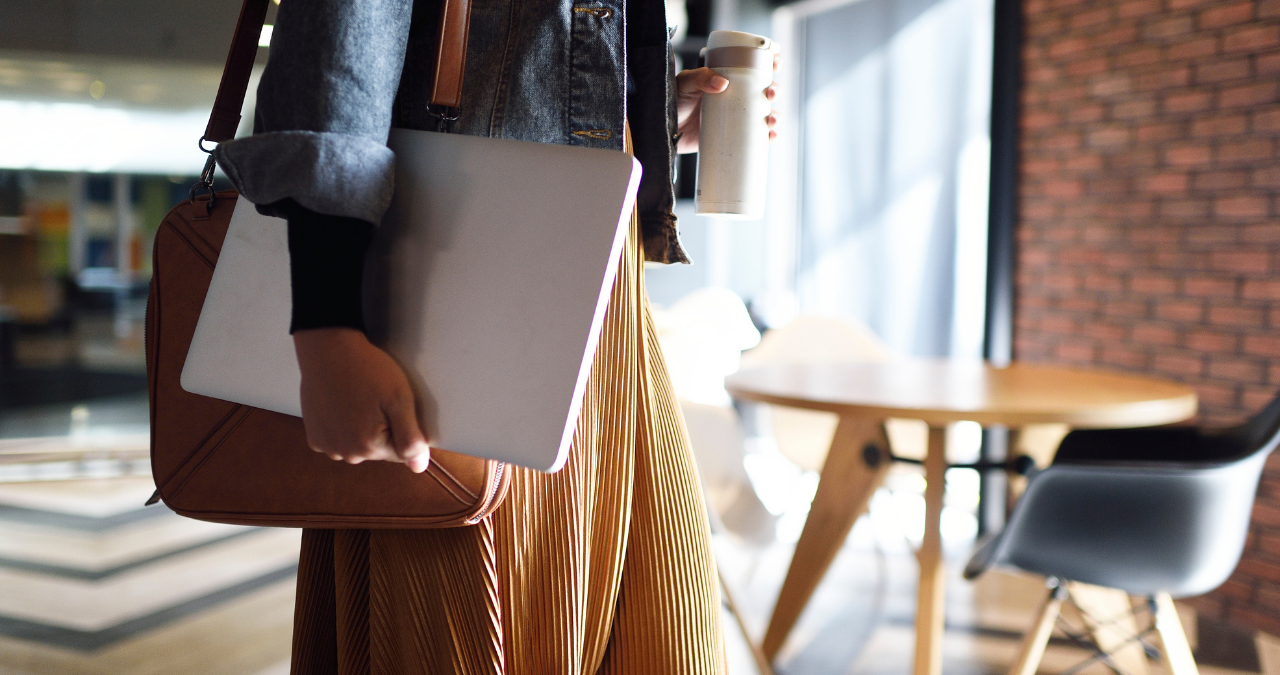 Woman returning to office carrying a laptop and mug.