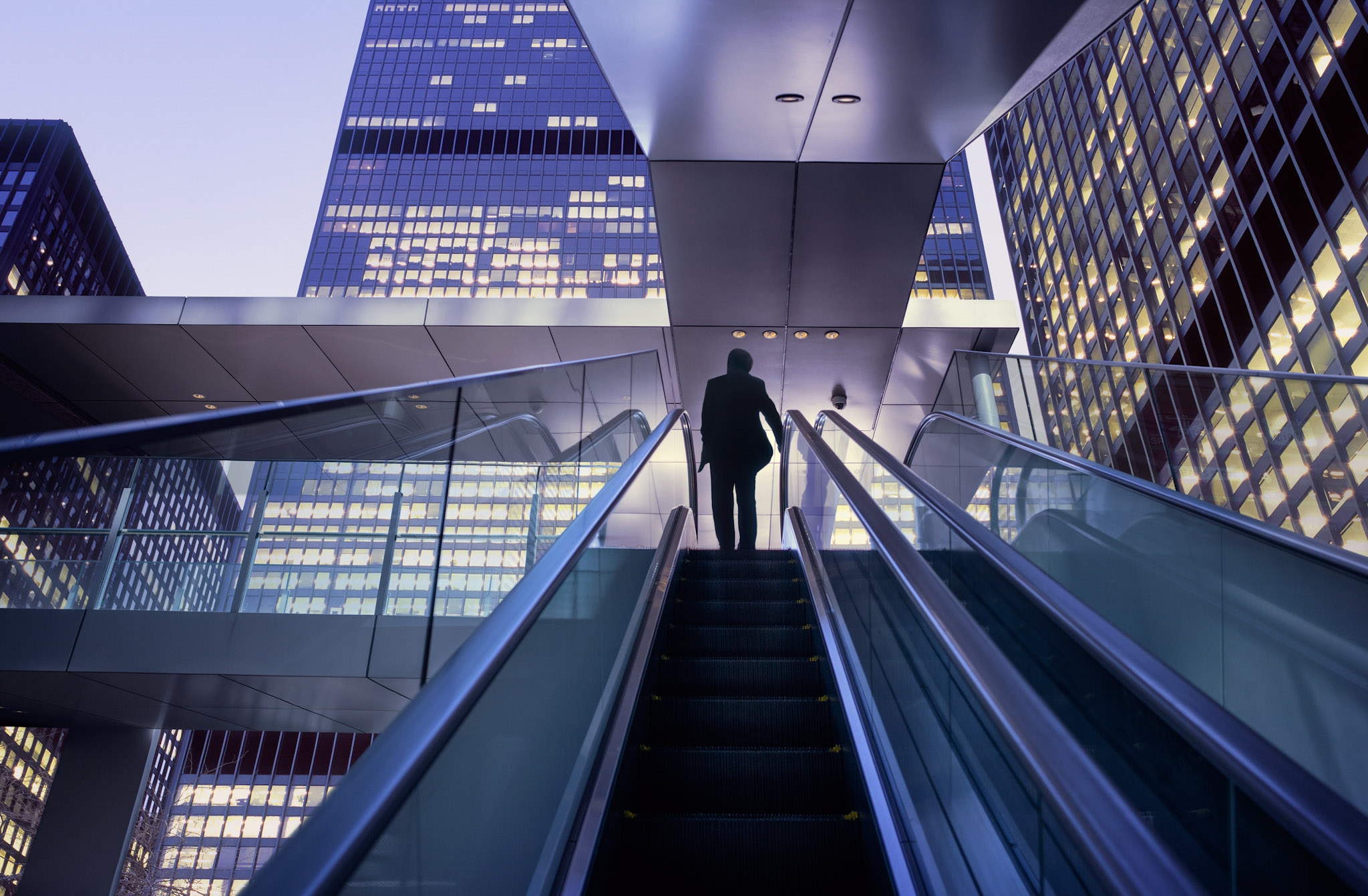 Business professional ascending escalator in a modern city, representing digital transformation and enterprise technology advancement.